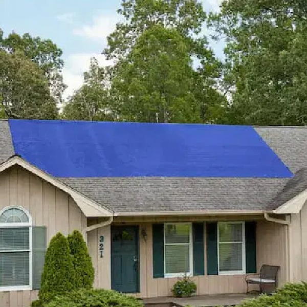 A blue tarp secured to a roof and covering a group of damaged shingles that had been allowing water inside.